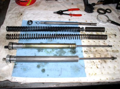 A comparison of fork internals. Top is the two-piece original spring, second down is a new Wirth progressive spring. Third down is an original damper cartridge and on the bottom the new FAC unit. Good thing we replaced the damper cartridges - this one leaks profusely when the rod is moved in and out. 